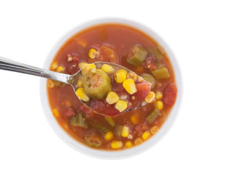 Top view of a spoonful of corn, okra and stewed tomatoes with the remainder of the vegetables in water with seasonings below isolated on a white background.の写真素材