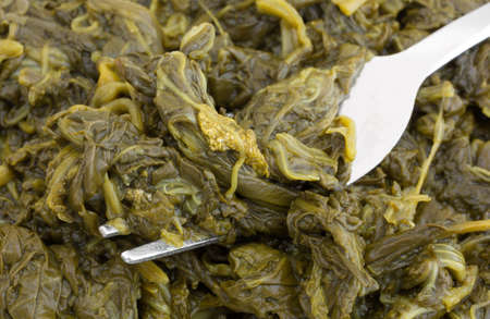 A very close view of canned spinach with a fork inserted into the food.
