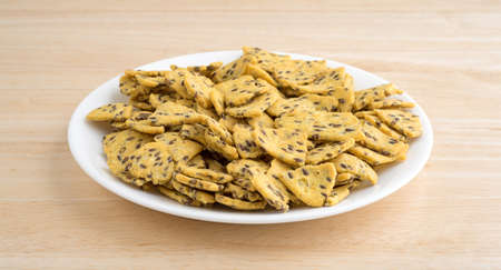 A portion of flax seed corn chips on a white plate atop a wood table top.