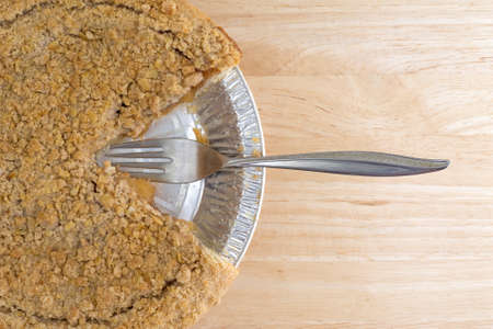 Top close view of a Dutch apple pie in a tinfoil baking dish on a wood table top with one slice...