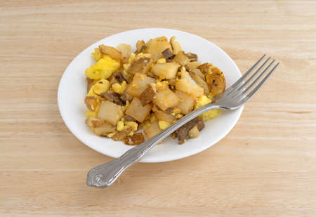 A breakfast meal on a plate with eggs, potatoes, cheese and steak with a fork to the side atop a wood table top.の写真素材