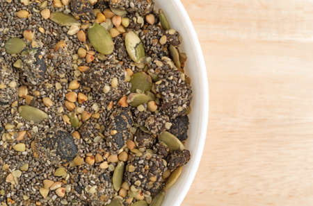 Top close view of a white bowl filled with chia, cranberry and pumpkin seeds breakfast cereal on a wood table.の写真素材