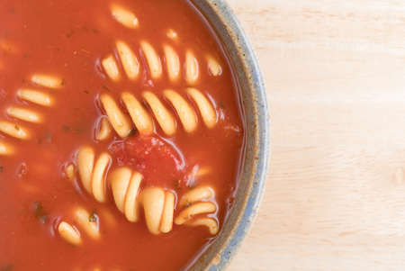Rotini tomato soup in an old stoneware bowl on a wood table top close view.の写真素材