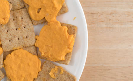 Top close view of several organic whole wheat crackers with cheese on a white plate atop a wood table.の写真素材