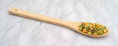 Side view of a portion of dry minestrone soup mix ingredients in a wood spoon atop a marble cutting board.の写真素材