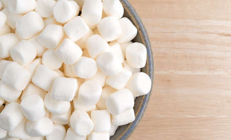Top close view of small bite size marshmallows filling an old stoneware bowl on a wood table.の写真素材