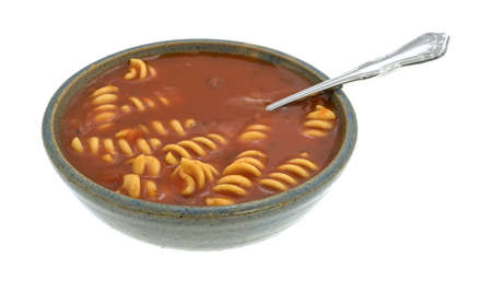 Rotini tomato soup in an old stoneware bowl with a spoon inserted into the food isolated on a white background.の写真素材