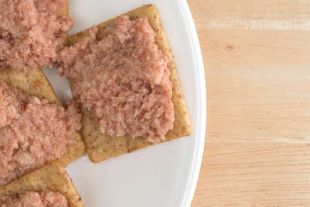 Top close view of a plate of deviled ham on wheat crackers atop a wood table.
