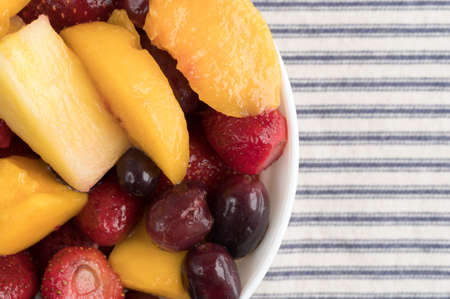 Top close view of a bowl of mixed fruit on a striped tablecloth.