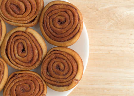 Top close view of several pecan sweet rolls on a white plate atop a wood table.