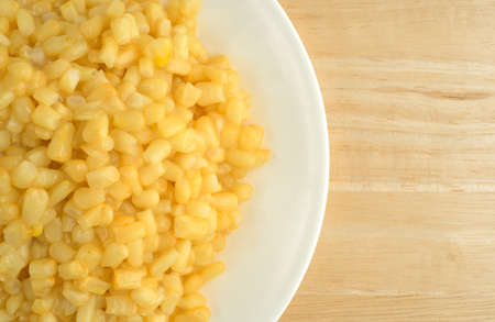 Top close view of shoepeg white corn with a butter sauce on a white plate atop a wood table.の写真素材
