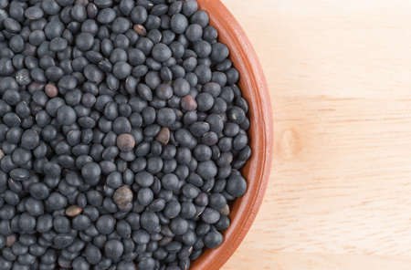 Top close view of a small bowl filled with black beluga lentils on a wood table.の写真素材