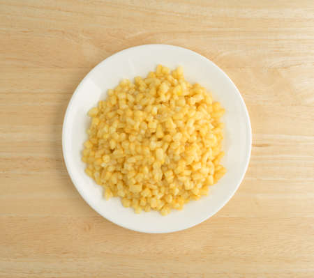 Top view of shoepeg white corn with a butter sauce on a white plate atop a wood table.の写真素材