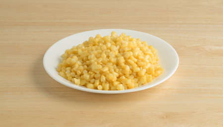 Shoepeg white corn with a butter sauce on a white plate atop a wood table.の写真素材