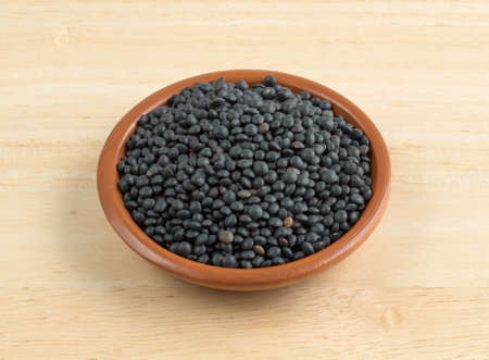 A small bowl filled with black beluga lentils on a wood table.の写真素材