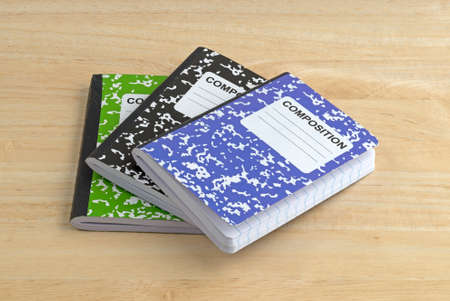 Three composition notebooks on a wood table.