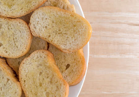 Top close view of a plate of crostini that has been dabbed with olive oil on a wood table.の写真素材