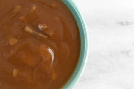 Top close view of a bowl of mushroom soup with small chunks of beef on a gray marble table.