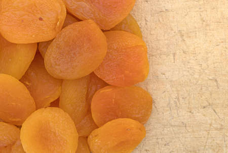 Top close view of several dried apricots on an old wood cutting board.の写真素材