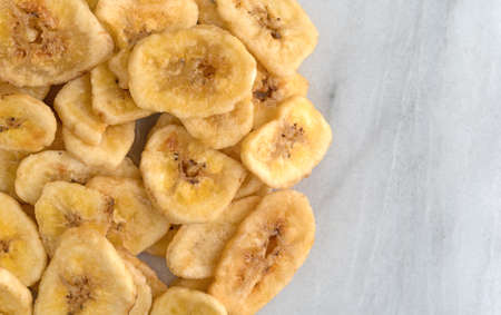 Close view of dehydrated banana chips on a gray marble cutting board.の写真素材