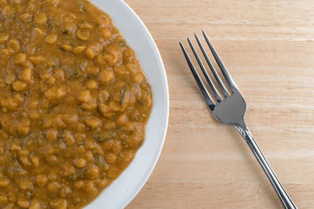 Top close view of a plate of spinach and yellow lentils in a gravy with a fork on a wood table top.