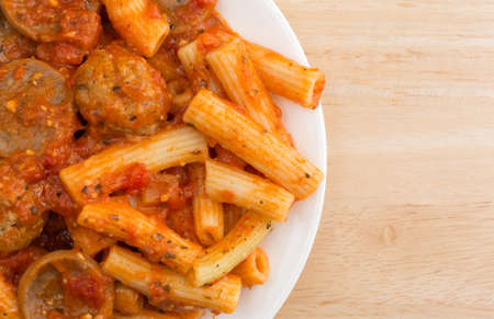 Top close view of a serving of rigatoni pasta with sausage and meatballs in a marinara sauce on a plate atop a wood table.の写真素材