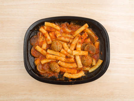 Top view of a TV dinner of rigatoni pasta with sausage and meatballs in a marinara sauce on a wood table.の写真素材