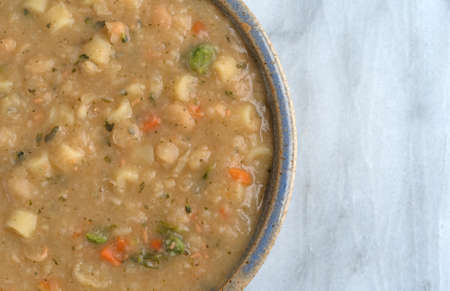 Top close view of a serving of white bean soup in an old stoneware bowl atop a marble table.の写真素材