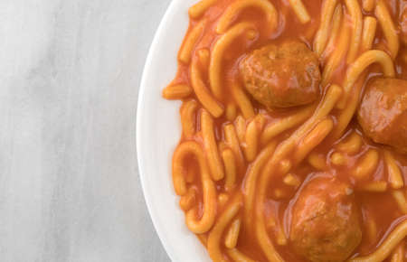 Top close view of a serving of spaghetti and meatballs on a white plate atop a gray marble table...
