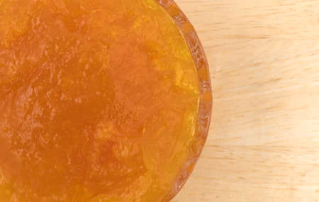 Top close view of sugar free apricot preserves in a small glass bowl atop a wood table.