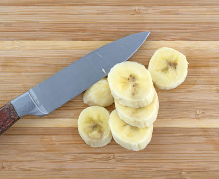 Top close view of sliced bananas on a wood cutting board with a knife.の写真素材