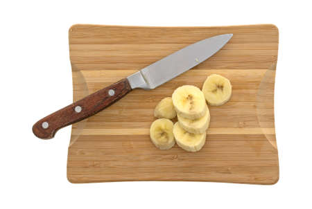 Top view of sliced bananas on a wood cutting board with a knife isolated on a white background.の写真素材