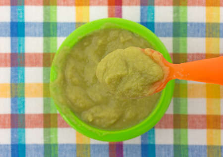 A serving of green peas baby food in a small bowl on a colorful place mat with a spoonful above.の写真素材
