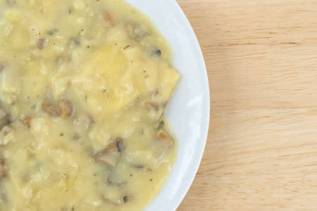 Top close view of ravioli covered with a cheese and mushroom sauce meal on a white atop a wood table.の写真素材