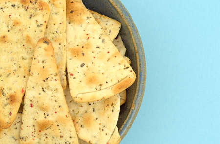 Top close view of pizza crust chips in an old stoneware bowl atop a blue fabric tablecloth.