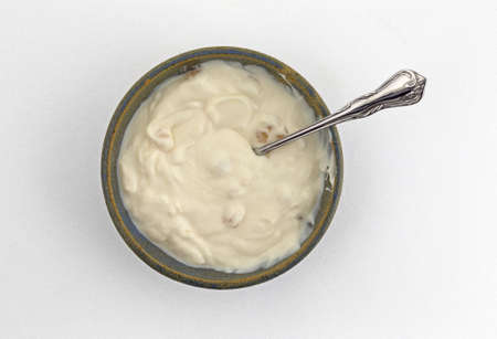 Top view of a large portion of apple vanilla Greek yogurt in an old stoneware bowl with a spoon in the food atop a white tablecloth.の写真素材