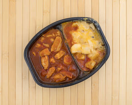 Top view of a TV dinner with chunks of chicken in a thick barbecue sauce plus cheese covered...