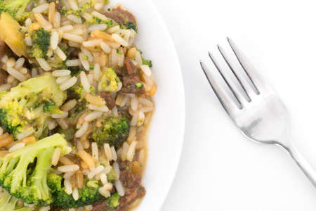 Top close view of a beef with broccoli and rice in a sauce on a plate with a fork to the side atop a white tablecloth.の写真素材
