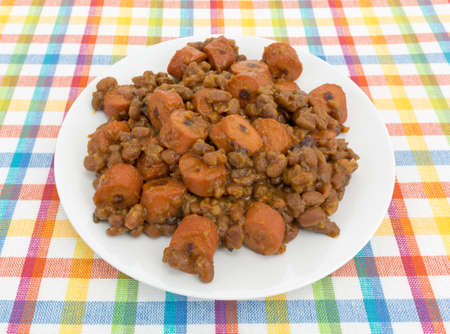 Baked beans and sliced hot dogs on a plate atop a colorful place mat.の写真素材
