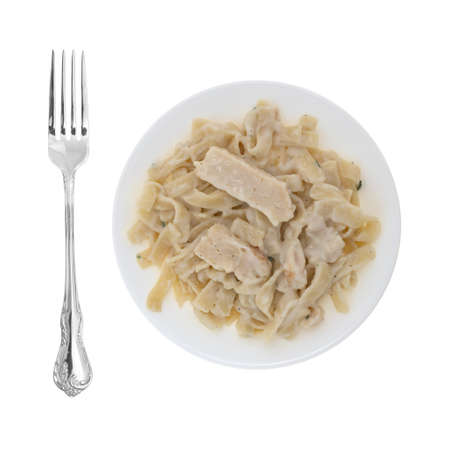 Top view of a plate with a serving of fettuccini with chicken and seasonings plus a fork to the side isolated on a white background.の写真素材