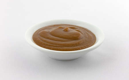 Side view of a small bowl filled with apple and prune puree baby food atop a white tablecloth.の写真素材