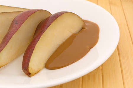 Close side view of slices of a red pear on a plate with peanut butter atop a wood plate mat.の写真素材