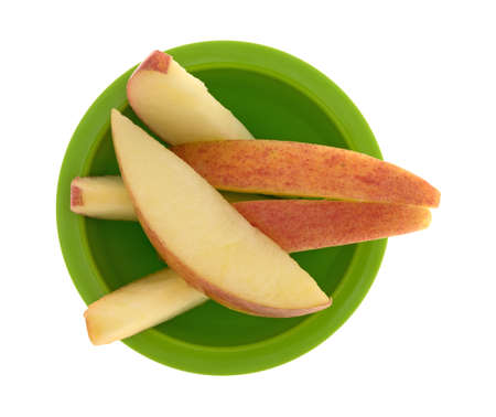 Top view of several slices of red apple in a small green bowl isolated on a white background.の写真素材