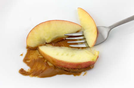 Three slices of red apple on a white plate with peanut butter plus a fork.の写真素材