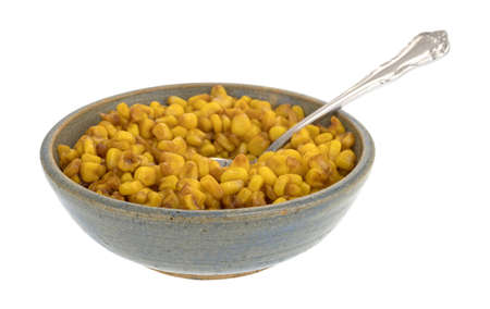 An old stoneware bowl filled with barbecue flavored cut corn and a spoon in the food isolated on a white background.の写真素材