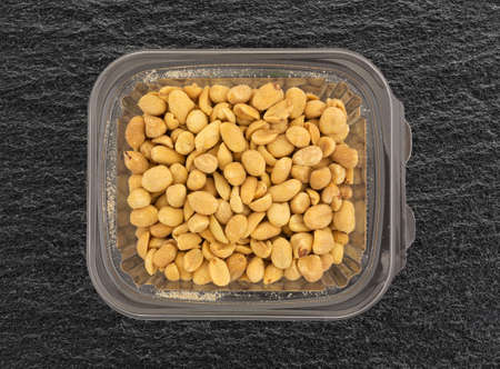 Top view of a container of barbecue flavored peanuts on a black slate table.の写真素材