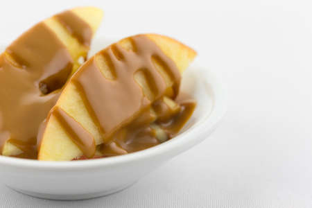 Slices of red apples covered with creamy peanut butter in a small bowl atop a white tablecloth.の写真素材