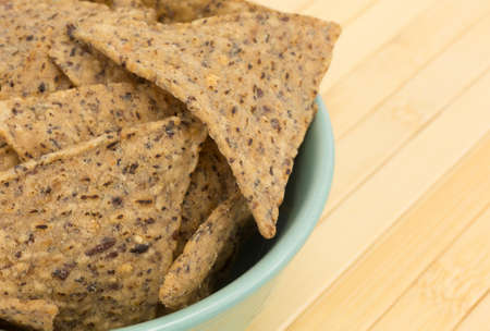 Side close view of a bowl filled with salt and pepper seasoned beans and rice chips on a wood place...