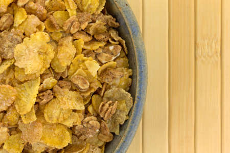 Top close view of an old stoneware bowl filled with dry multigrain breakfast cereal on a wood place...
