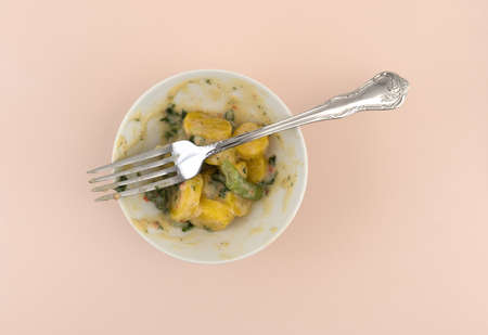 Top view of an almost finished bowl of yellow carrots and green beans in a parmesan cheese sauce with a fork atop a pink stone table top.の写真素材